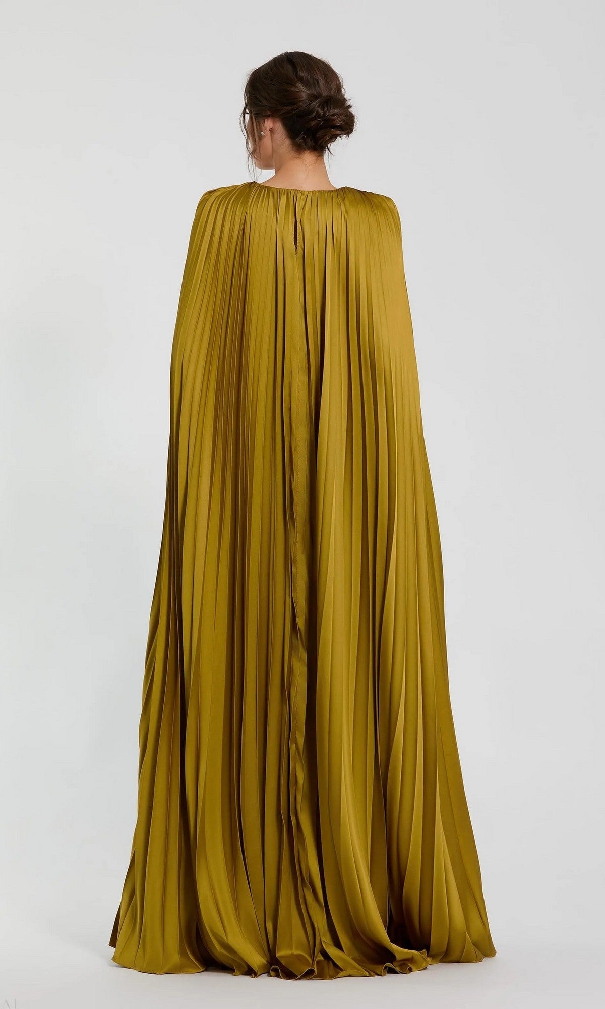 A woman with dark hair in an updo is seen from the back wearing the Mac Duggal 49872 long formal dress—a pleated, golden-yellow charmeuse gown with an A-line skirt and cape detailing—against a plain light background.